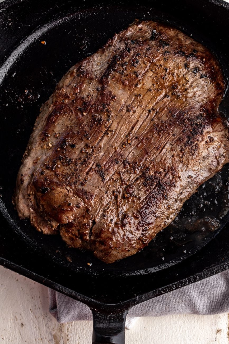 seared flank steak in cast iron pan.