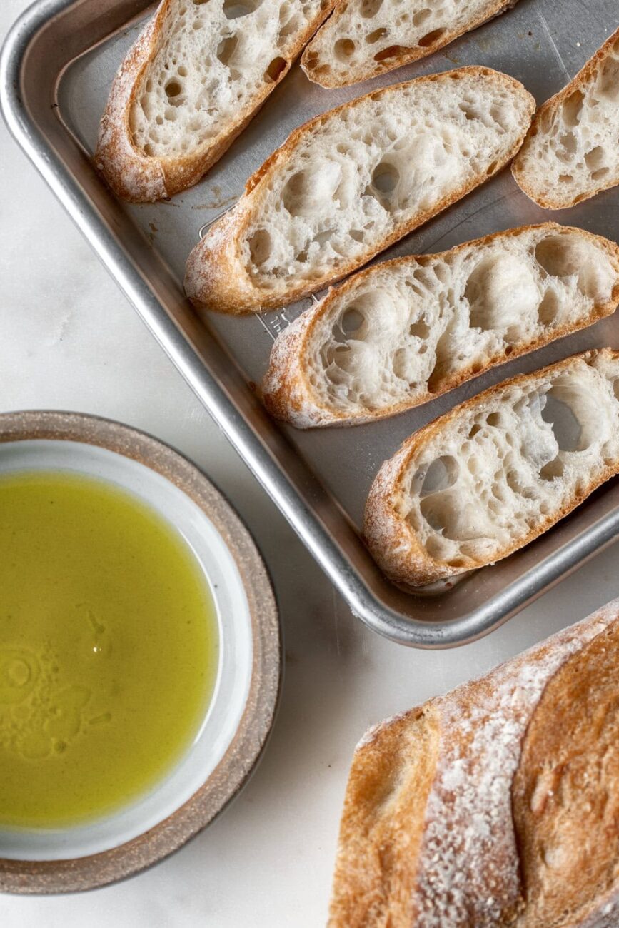 Bread on sheet pan with olive oil dish on the side.