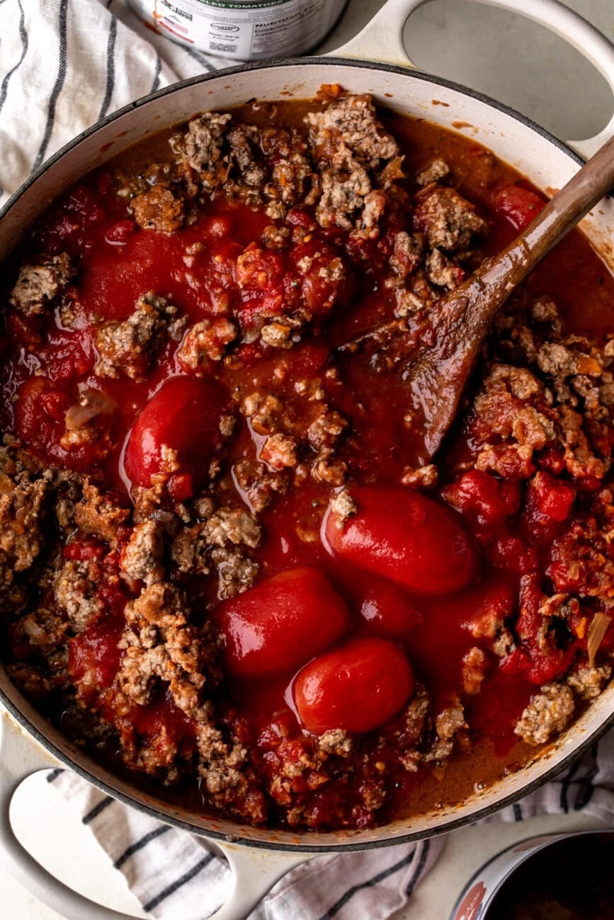 bolognese ingredients simmering on stove with peeled tomatoes.