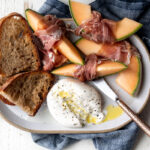 burrata and prosciutto snack plate with cantaloupe and toasted garlic bread.