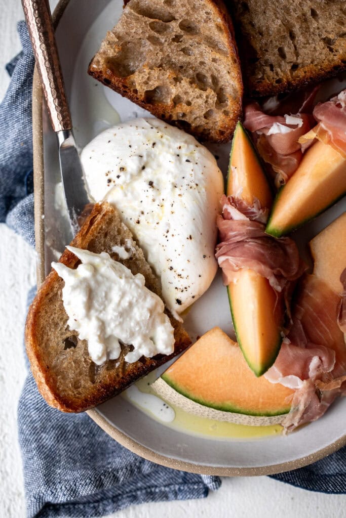 burrata and prosciutto snack plate with cantaloupe and toasted garlic bread cut burrata cheese.