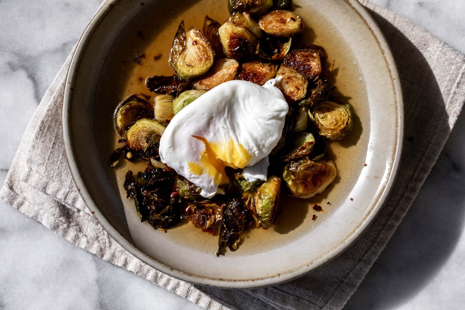 roasted brussels sprouts in a light bacon dashi broth with a poached egg split open in stone bowl.