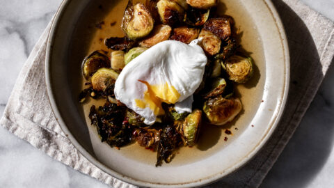 roasted brussels sprouts in a light bacon dashi broth with a poached egg split open in stone bowl