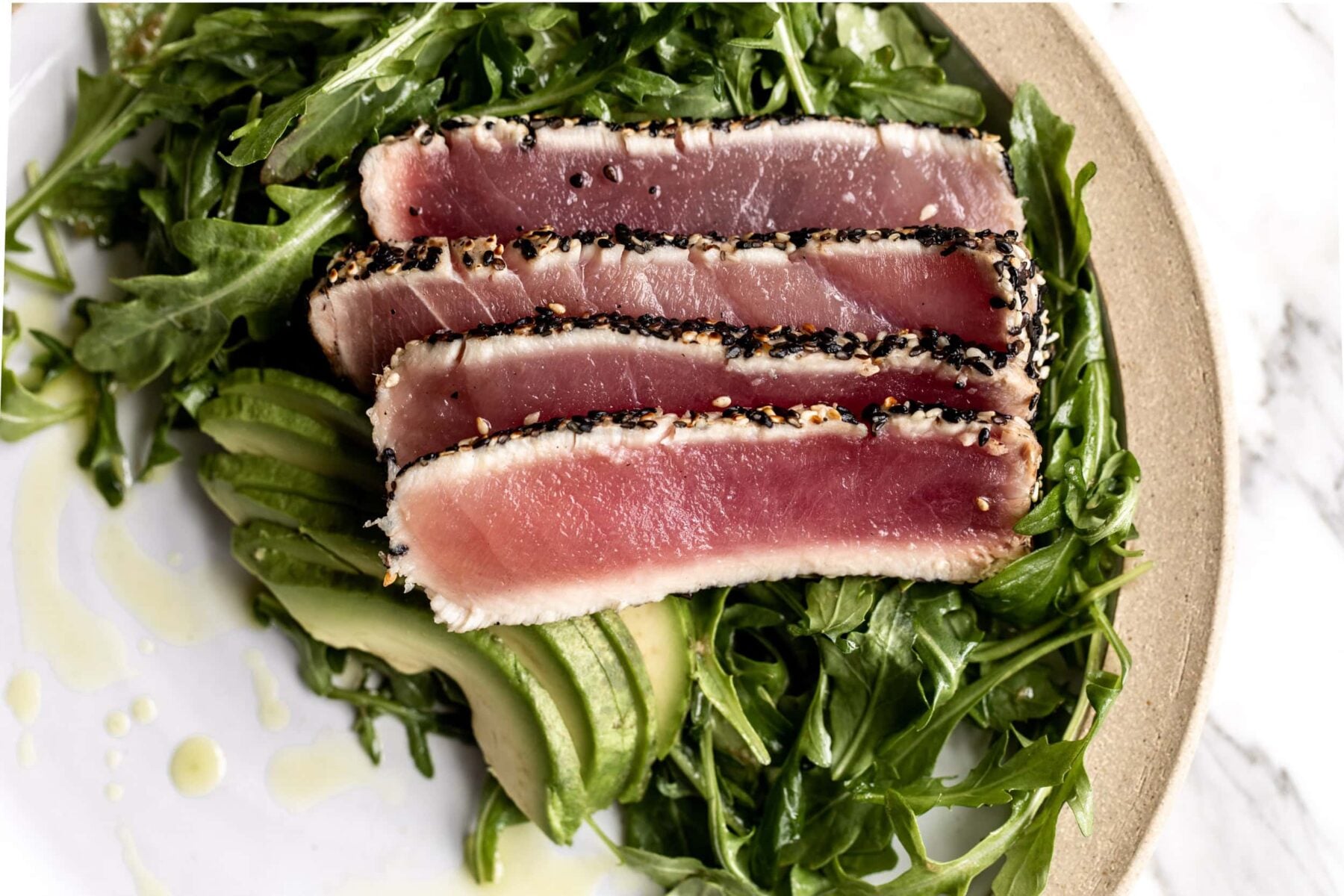slices of seared sesame crusted ahi tuna over a bed of arugula and sliced avocado.