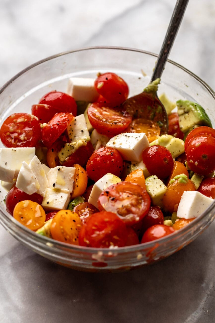 tomato avocado mozzarella salad marinated in bowl.