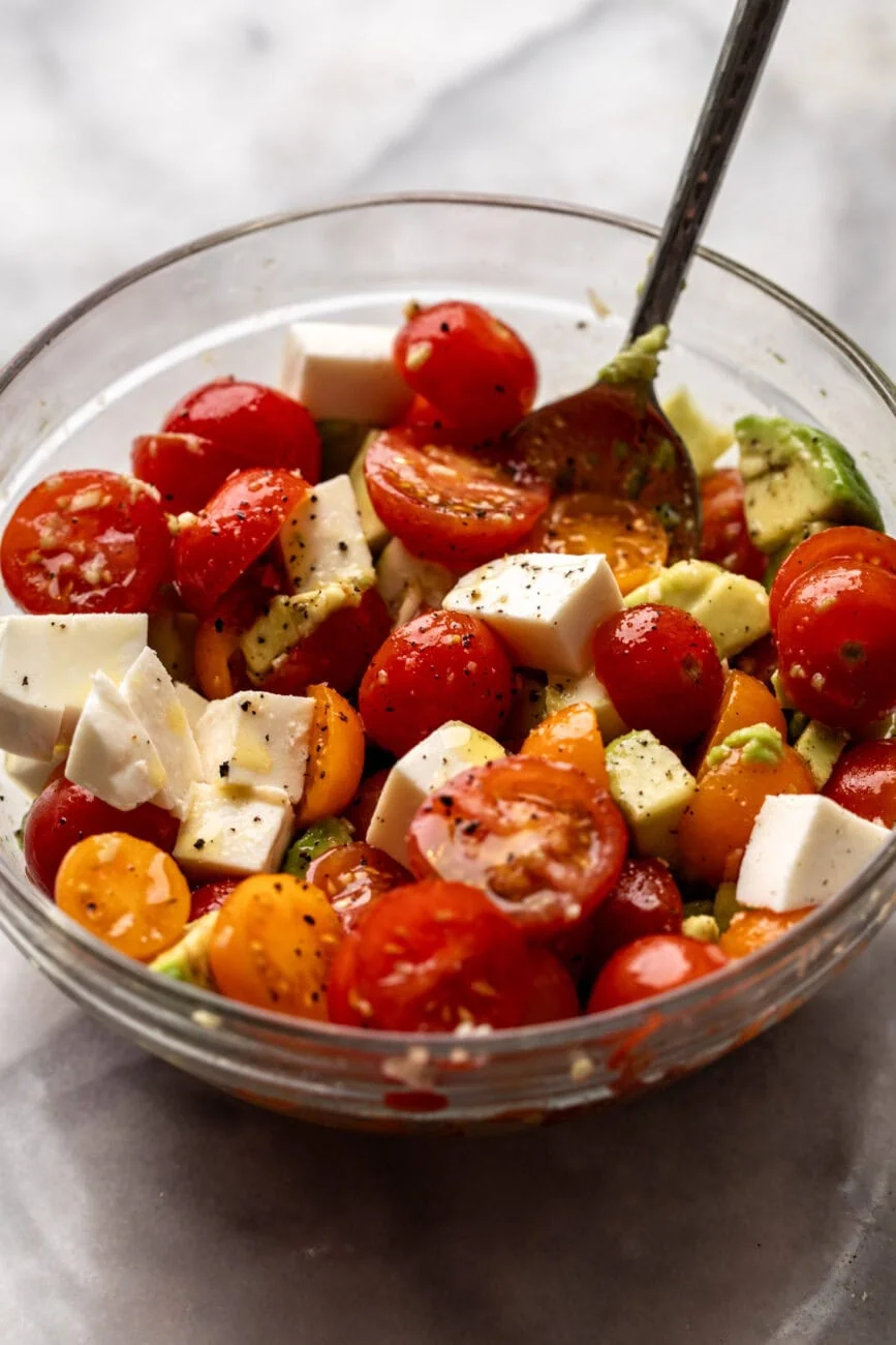tomato avocado mozzarella salad marinated in bowl.