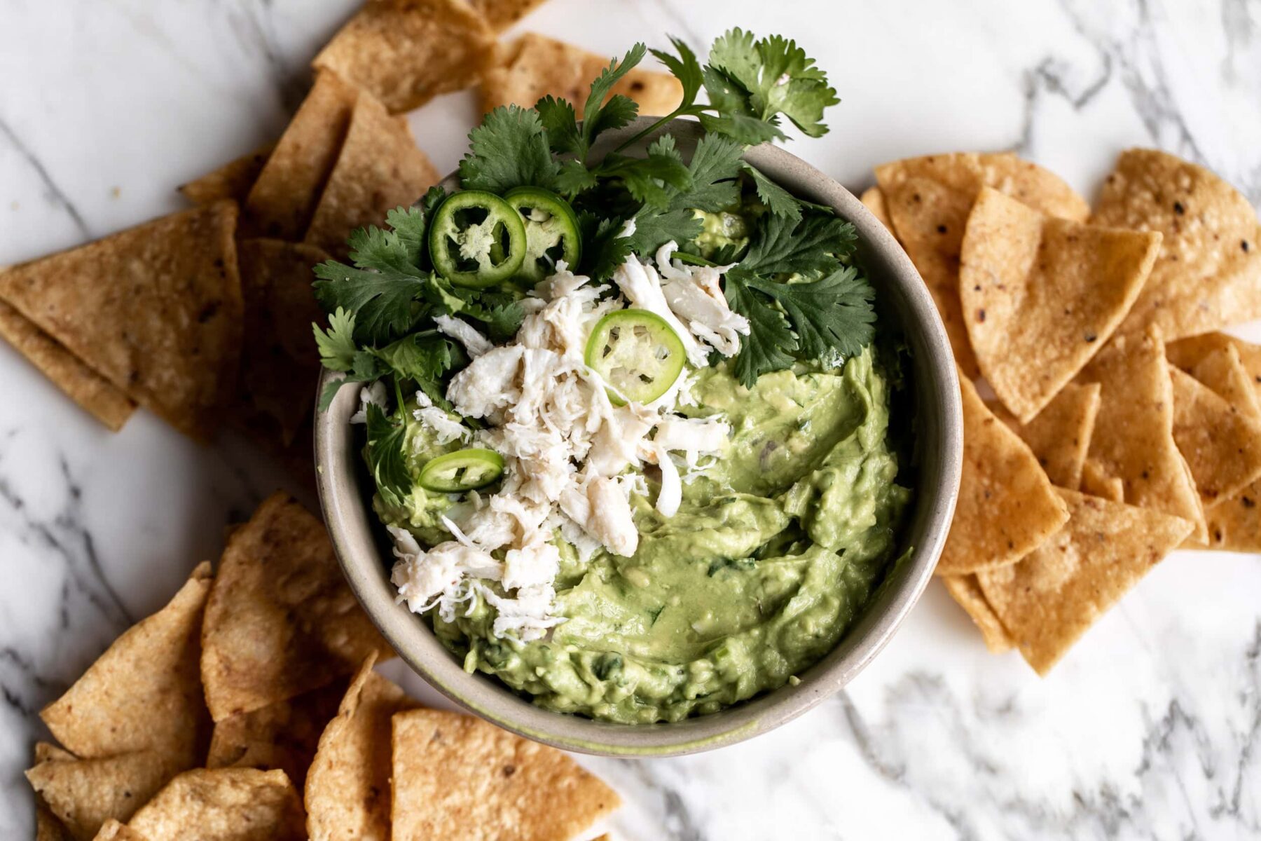 bowl of guacamole with crab and cilantro with tortilla chips.