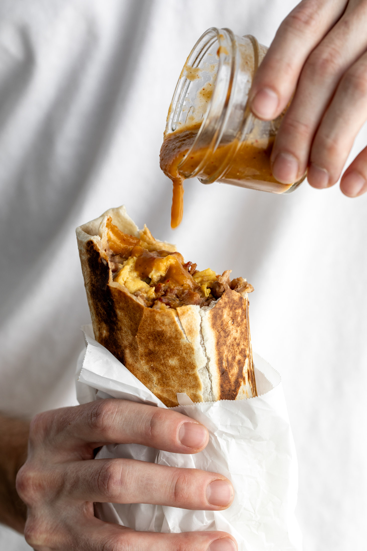 bacon breakfast burrito with hot sauce dripping onto bean, cheese egg and bacon filling.