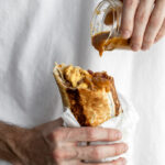 bacon breakfast burrito with hot sauce dripping onto bean, cheese egg and bacon filling.