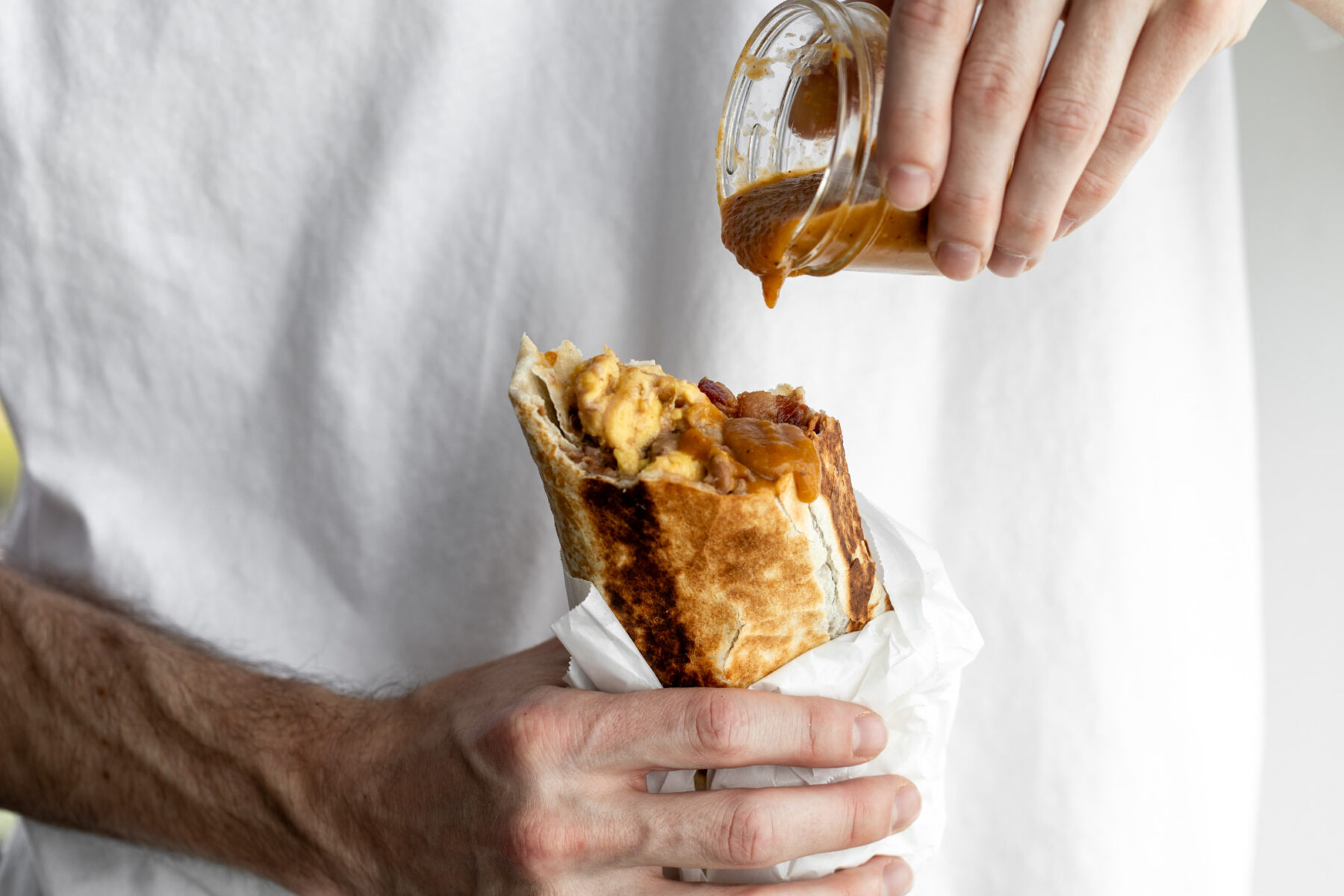 bacon breakfast burrito with hot sauce dripping onto bean, cheese egg and bacon filling.