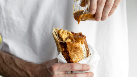 bacon breakfast burrito with hot sauce dripping onto bean, cheese egg and bacon filling.