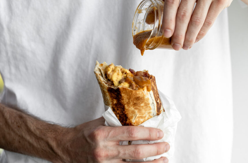 bacon breakfast burrito with hot sauce dripping onto bean, cheese egg and bacon filling.