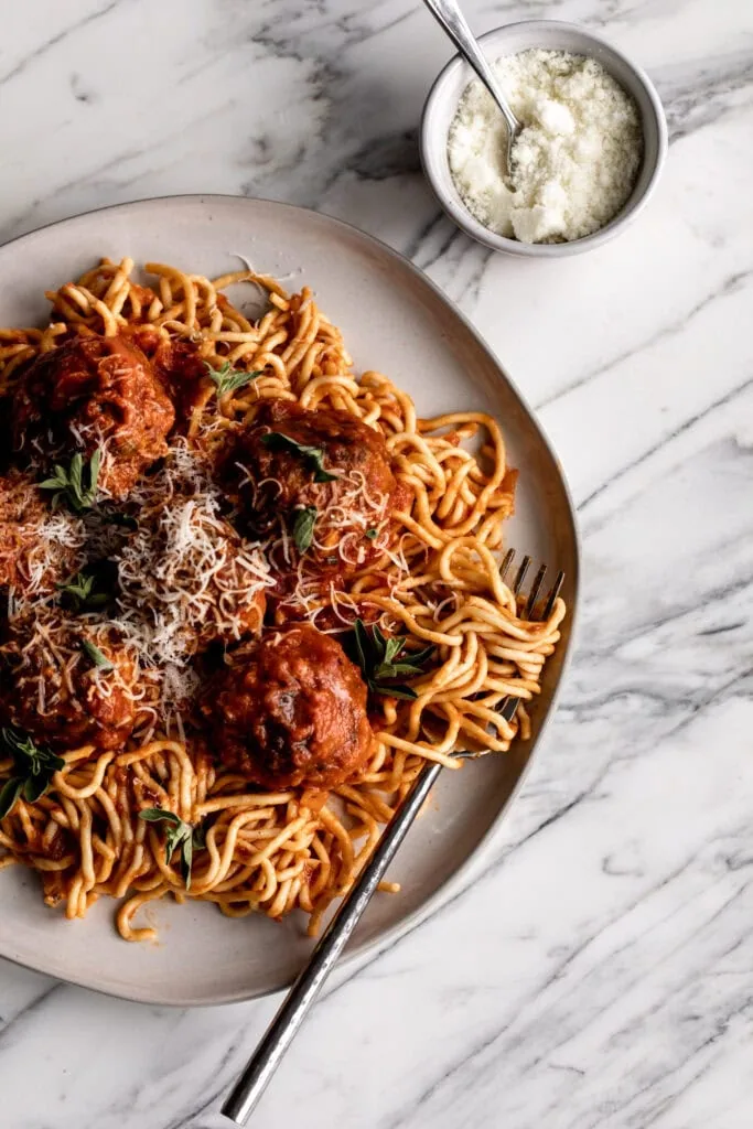 beef, pork and prosciutto meatballs on plate over spaghetti with marinara sauce and parmesan cheese