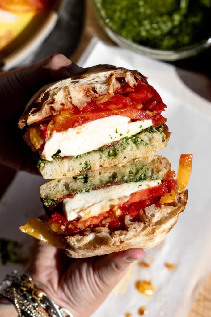 cut caprese sandwich with tomatoes mozzarella and pesto.