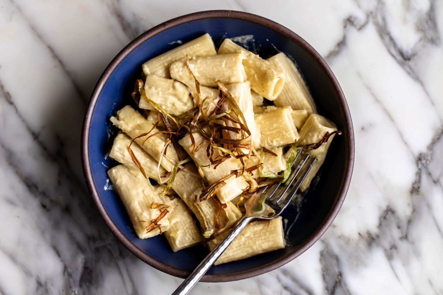 creamy corn pasta with frizzled leeks and truffle in a blue stone bowl on marble.