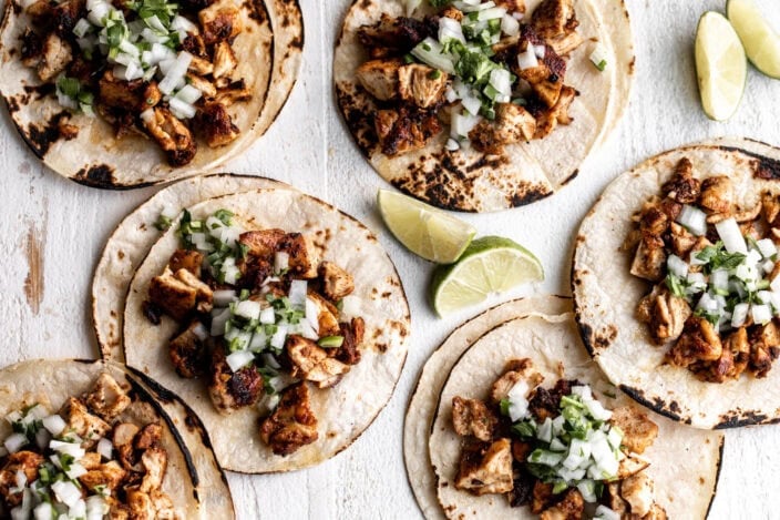Mexican chicken street tacos on corn tortillas with onion salsa and limes.
