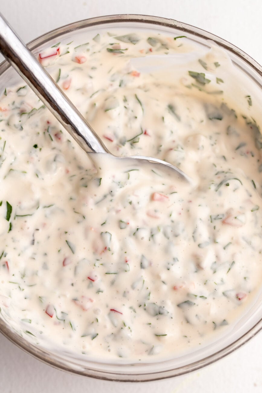 chimichurri aioli whisked with herbs in bowl.