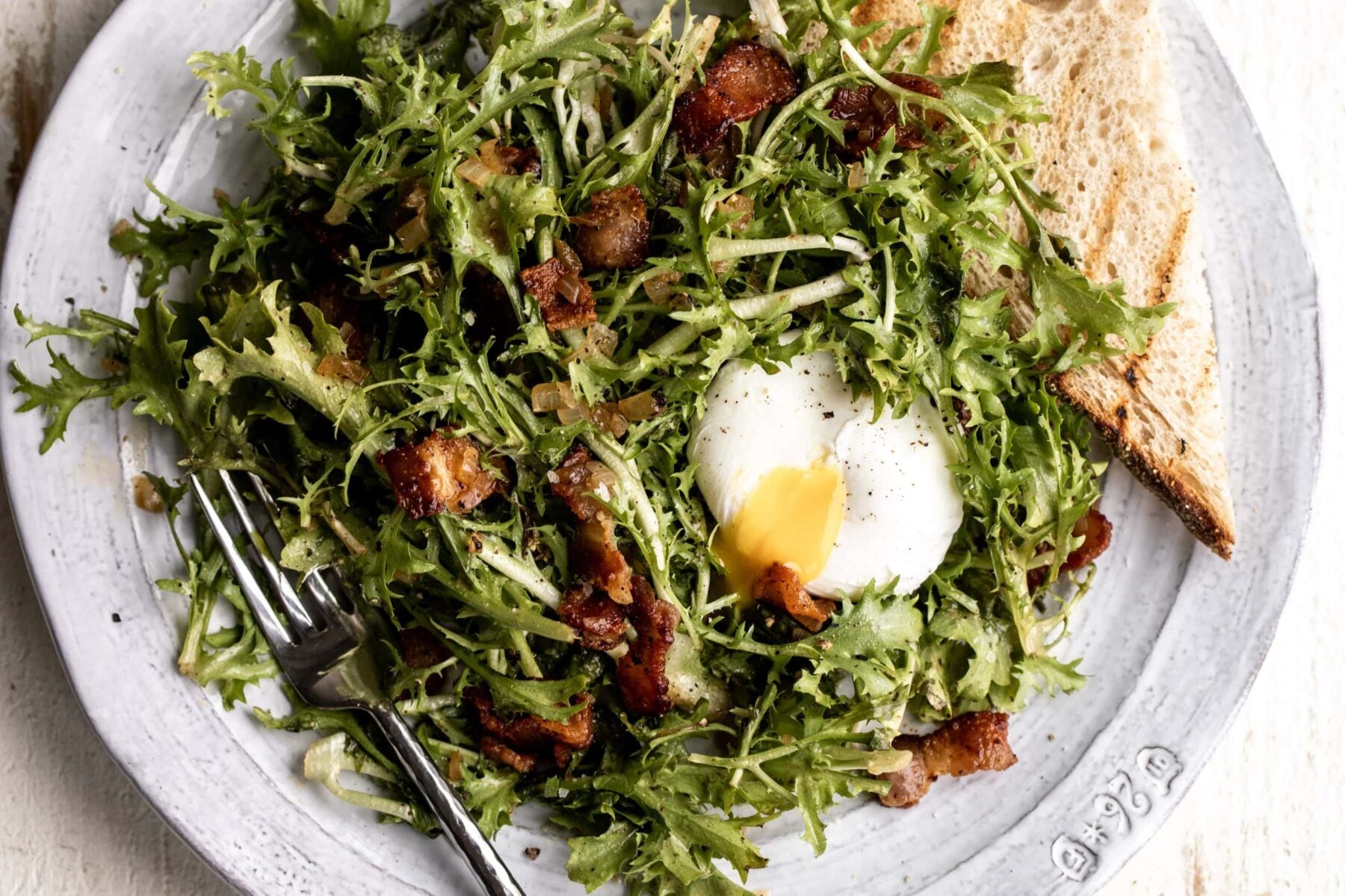 bacon and frisée French salad with a poached egg split open.