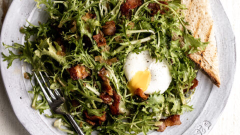 bacon and frisée French salad with a poached egg split open closeup