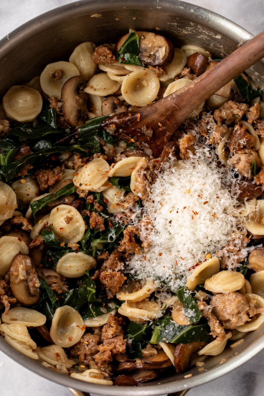 sausage pasta with collard greens and mushrooms topped with Parmesan cheese.