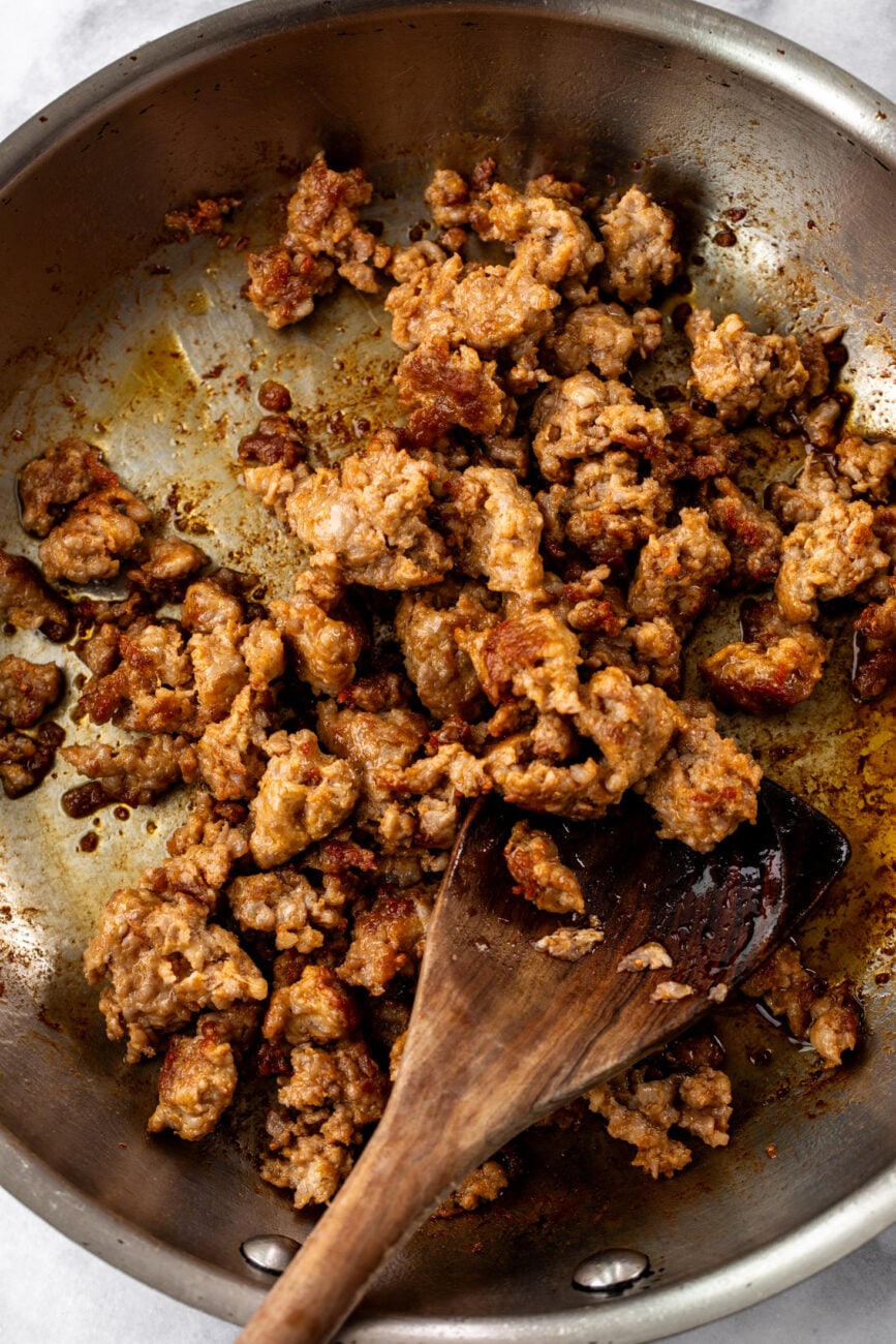 cooked italian sausage in pan with wooden spoon.