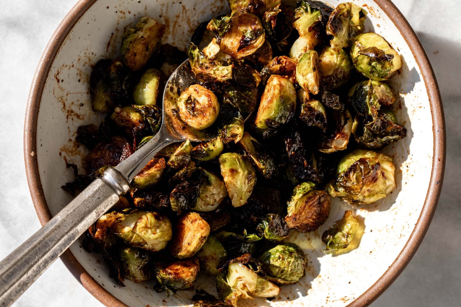 Balsamic Sriracha Roasted Brussels Sprouts in stone bowl with serving spoon.