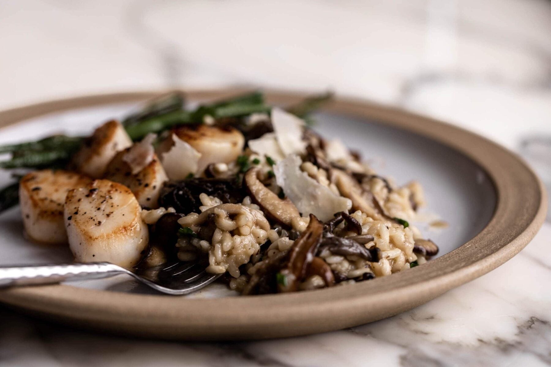 mixed mushroom risotto on ceramic plate with green beans and sautéed scallops.