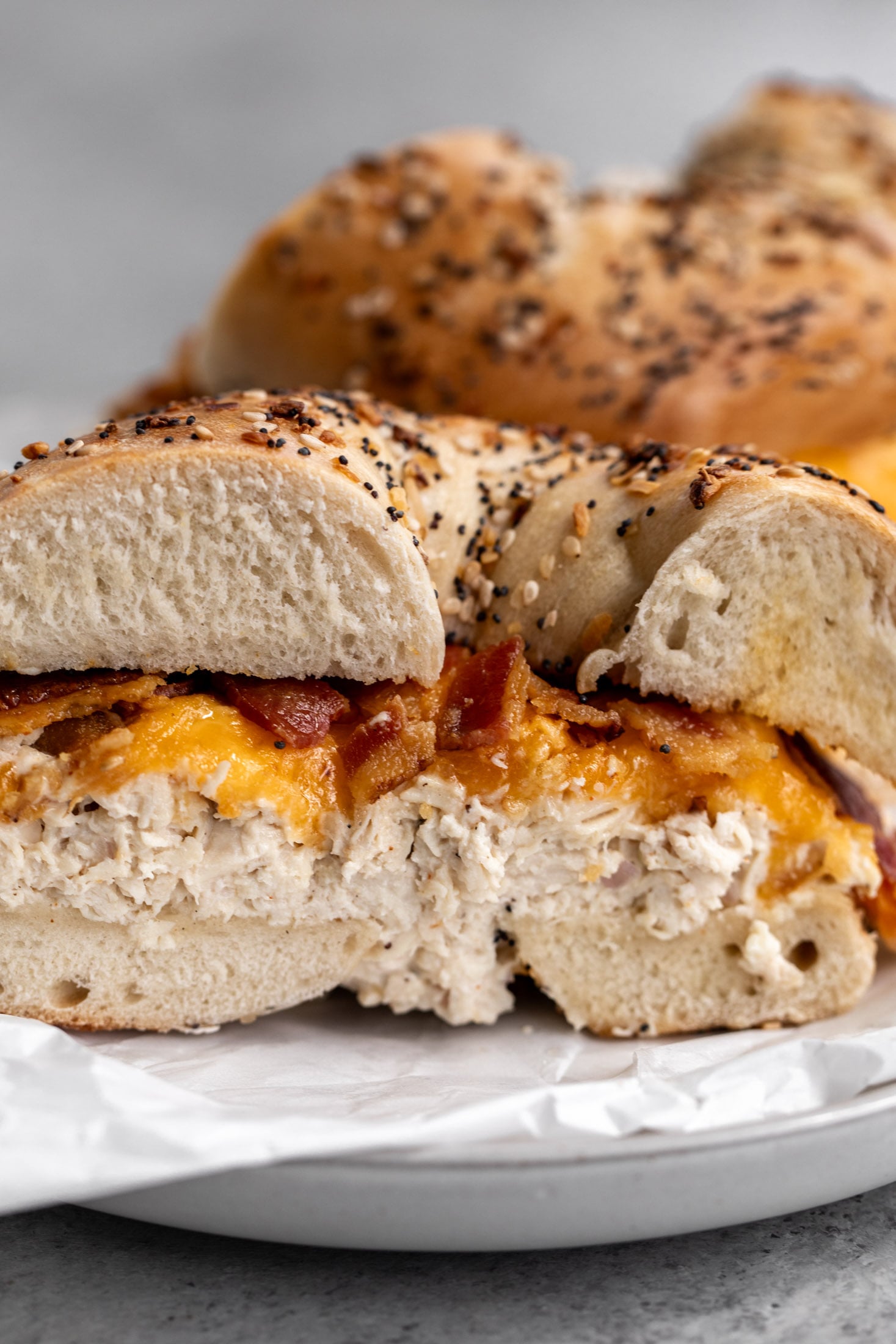 Chicken salad sandwich on bagel with melted cheddar cheese and bacon.