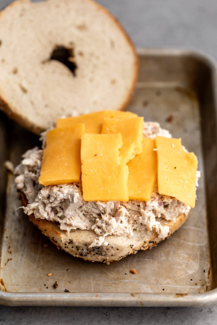 chicken salad spread on a bagel topped with slices of cheddar cheese.