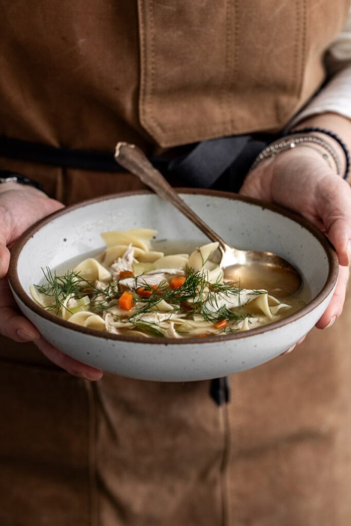 holding bowl of chicken noodle soup in hands.