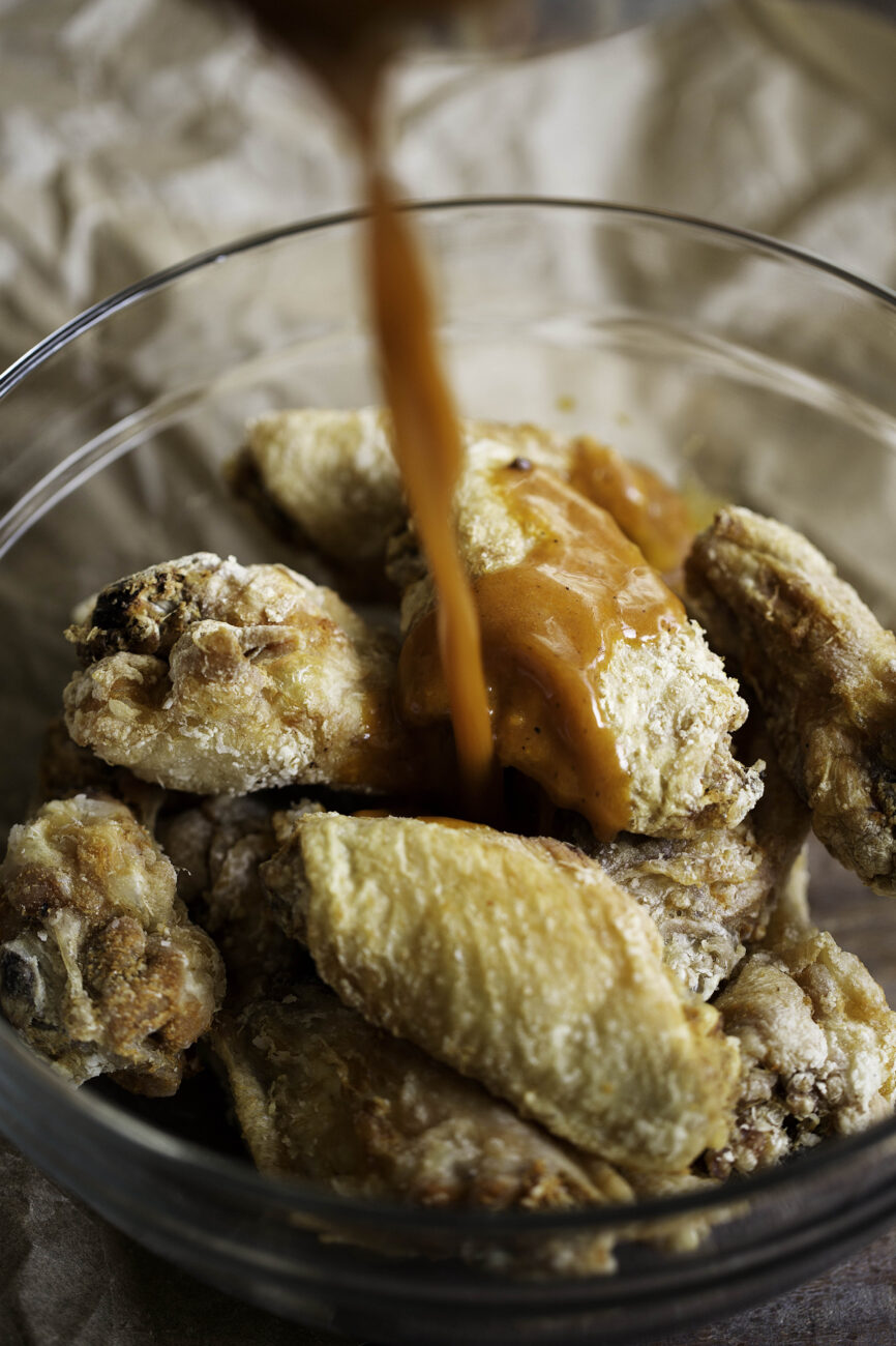 fried chicken wings tossed in homemade buffalo sauce in glass bowl.