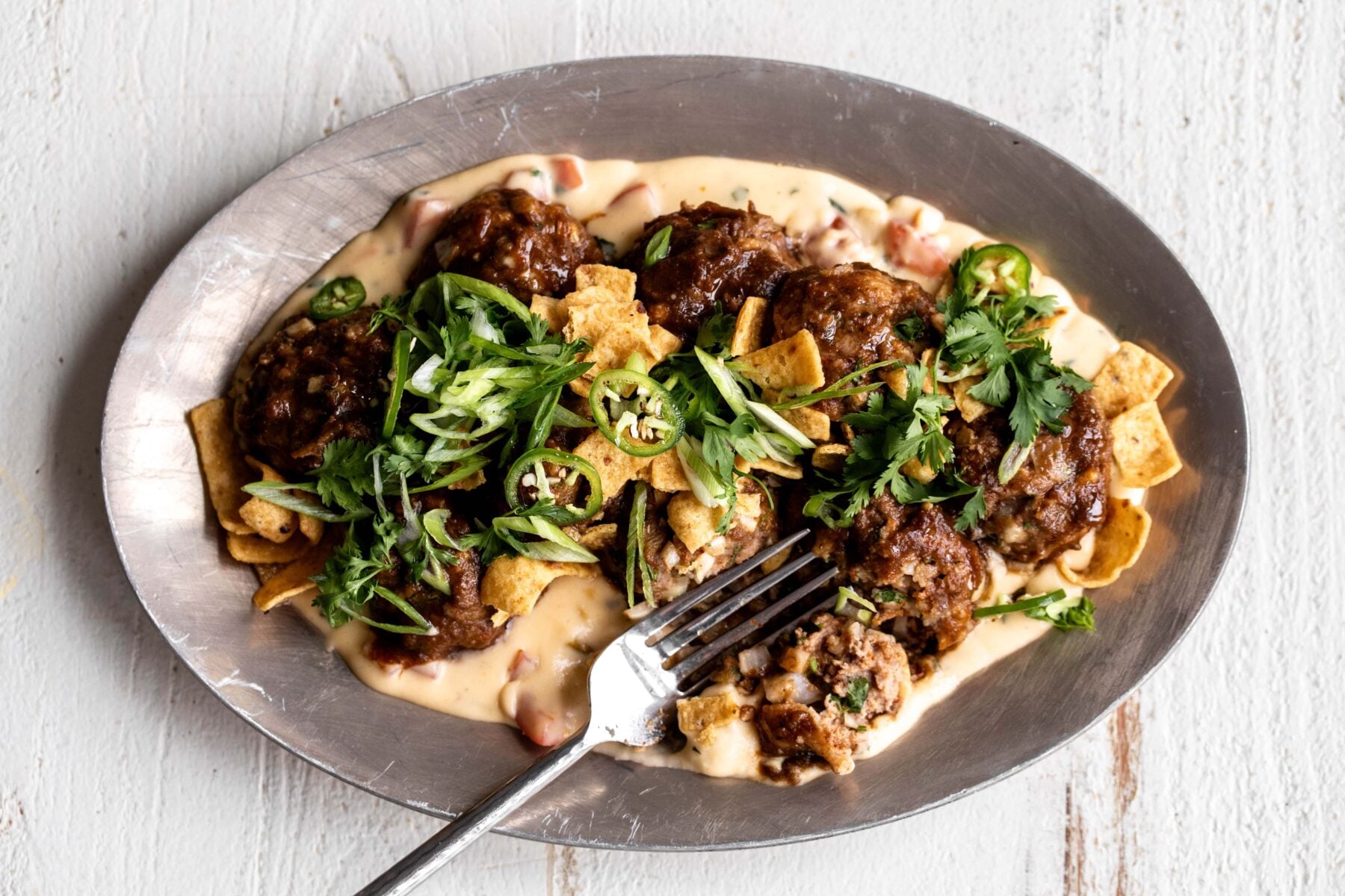 BBQ meatballs in charred scallion Barbecue sauce over queso with fritos corn chips scallions and cilantro.