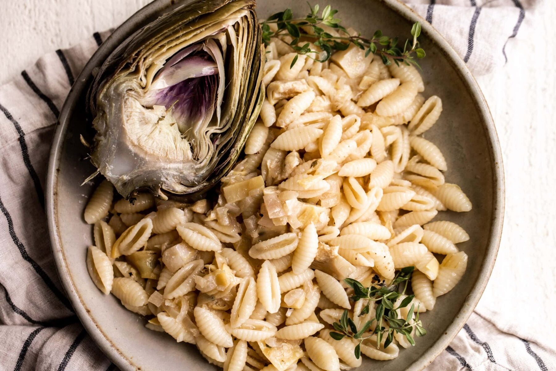 lemon artichoke pasta made with cavatelli with a half artichoke topped with parmesan cheese.