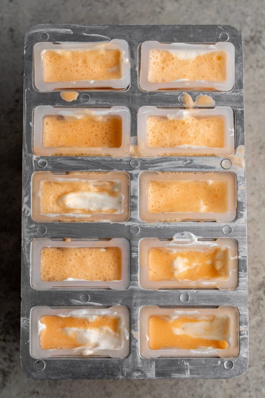 filled ice pop molds with alternating orange mixture and yogurt.