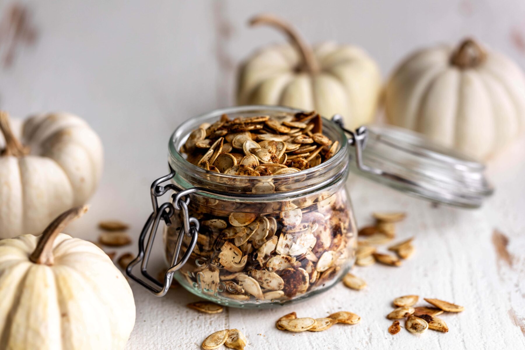 roasted ranch pumpkin seeds in a glass jar with small mini white pumpkins.