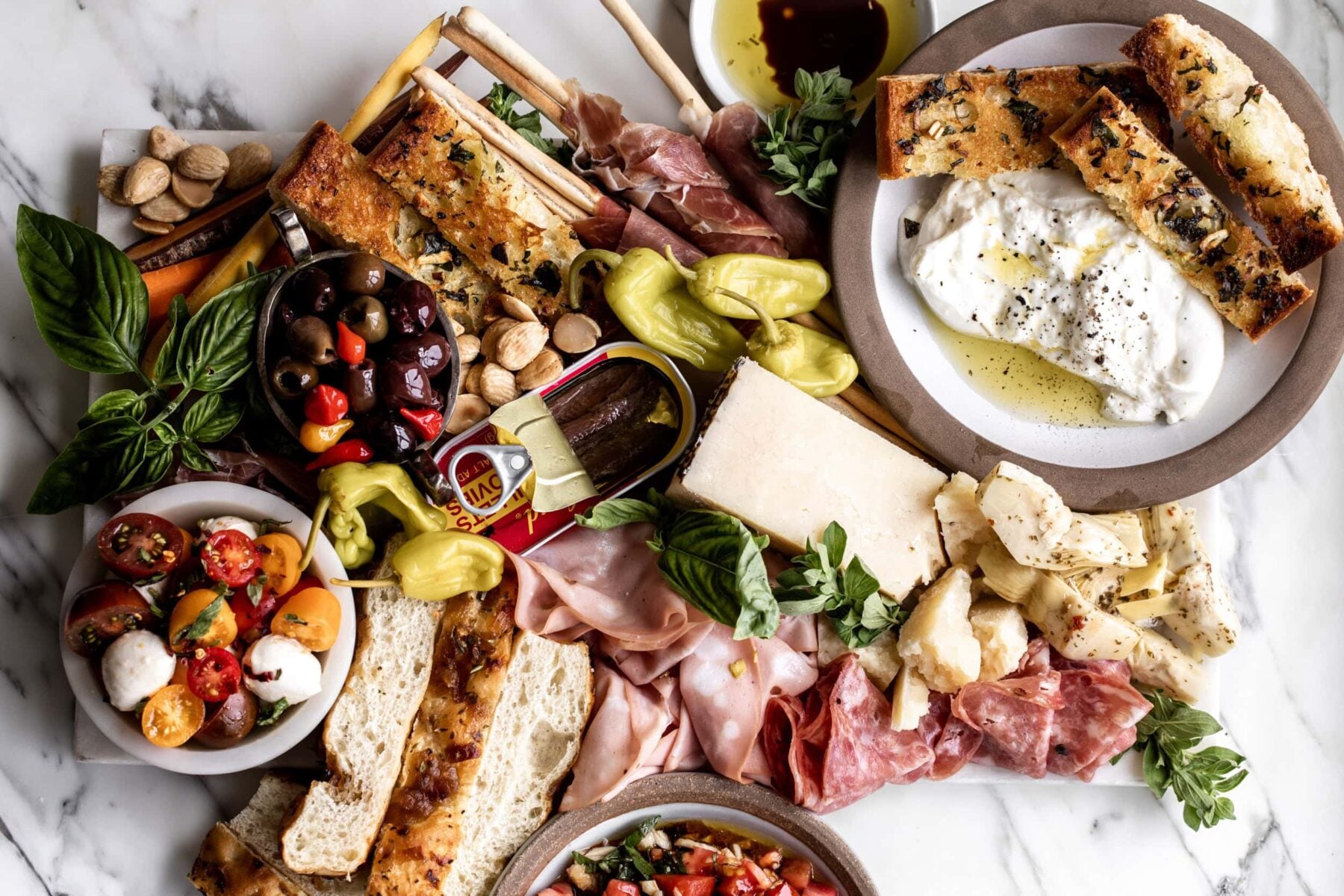 italian antipasto platter recipe with burrata, bruschetta, marinated tomato salad, pepperoncini, mortadella, prosciutto wrapped breadsticks.