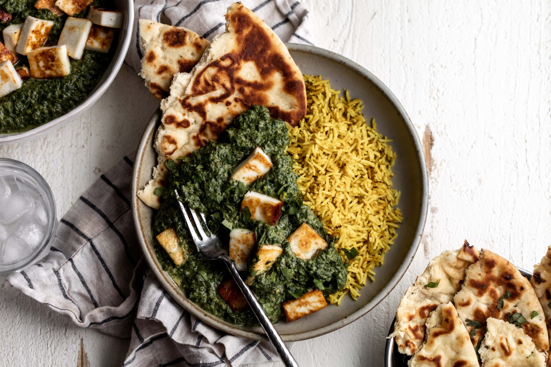 saag paneer over yellow turmeric rice with naan bread.