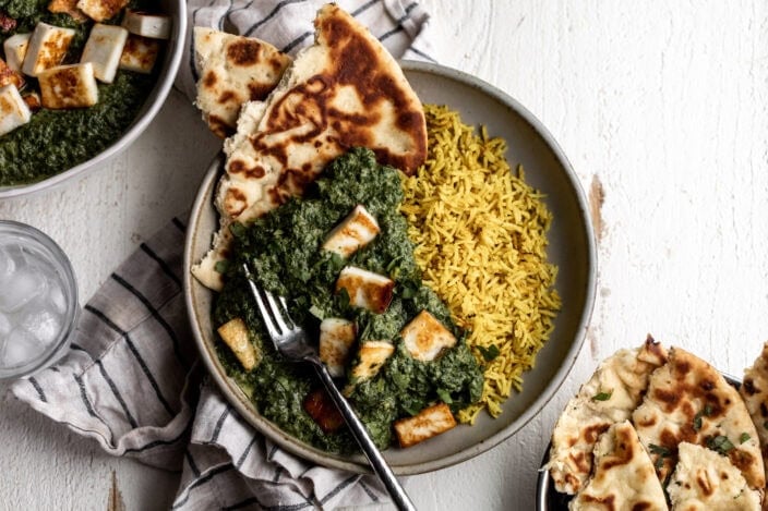 saag paneer over yellow turmeric rice with naan bread.