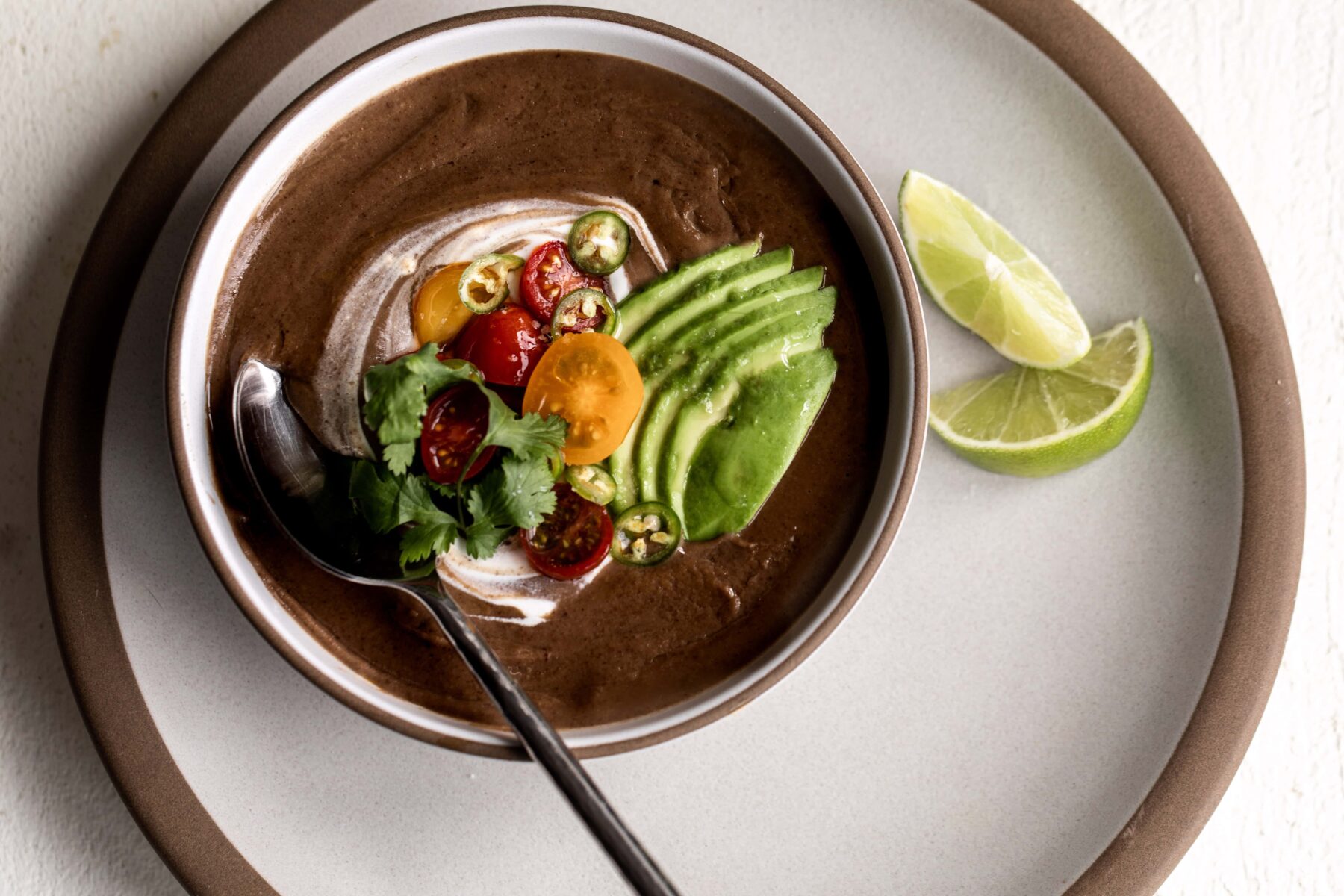Black bean soup with tomato and avocado topping with lime wedges.