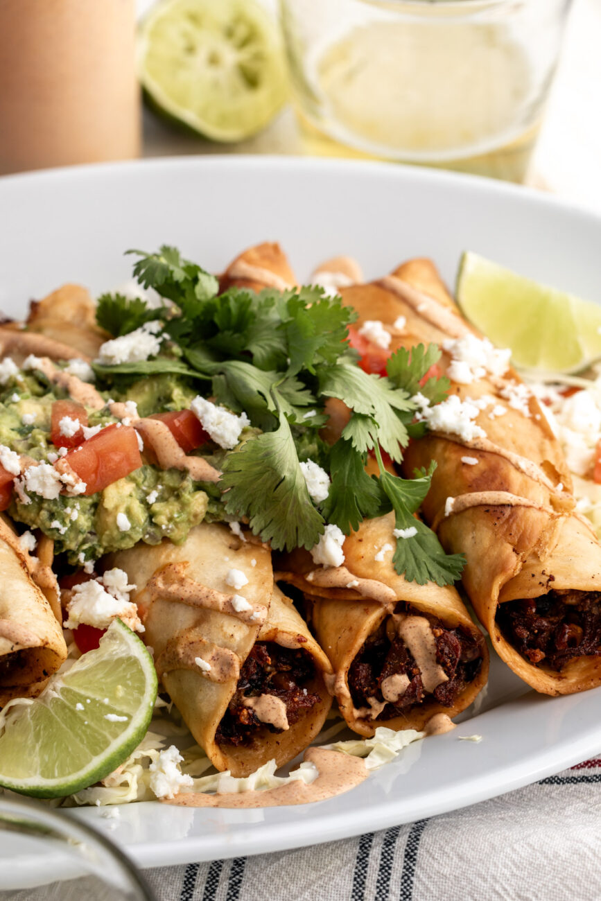 chicken flautas with mushroom and roasted corn with chipotle mayonnaise topped with guacamole diced tomatoes and cilantro.