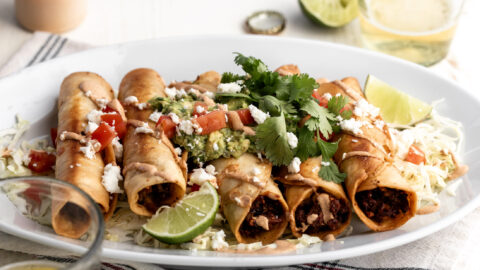 chicken flautas with mushroom and roasted corn with chipotle mayonnaise topped with guacamole diced tomatoes and cilantro.