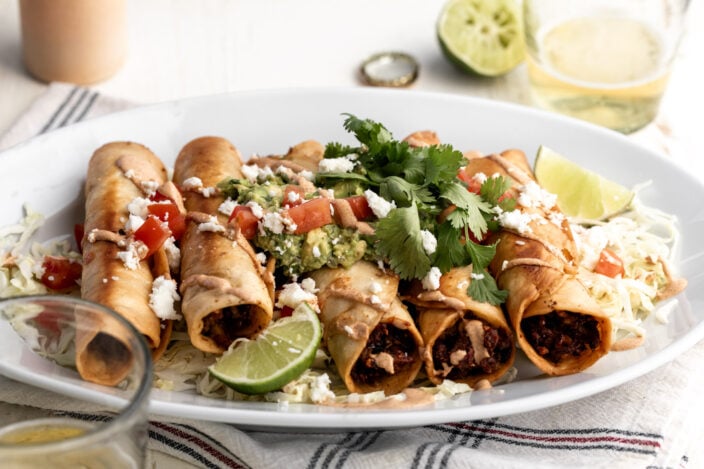 chicken flautas with mushroom and roasted corn with chipotle mayonnaise topped with guacamole diced tomatoes and cilantro.