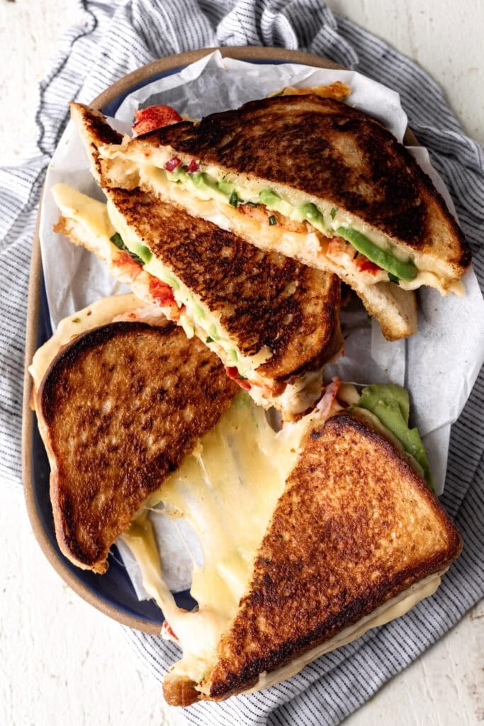 lobster grilled cheese served on plate with cheese pull.