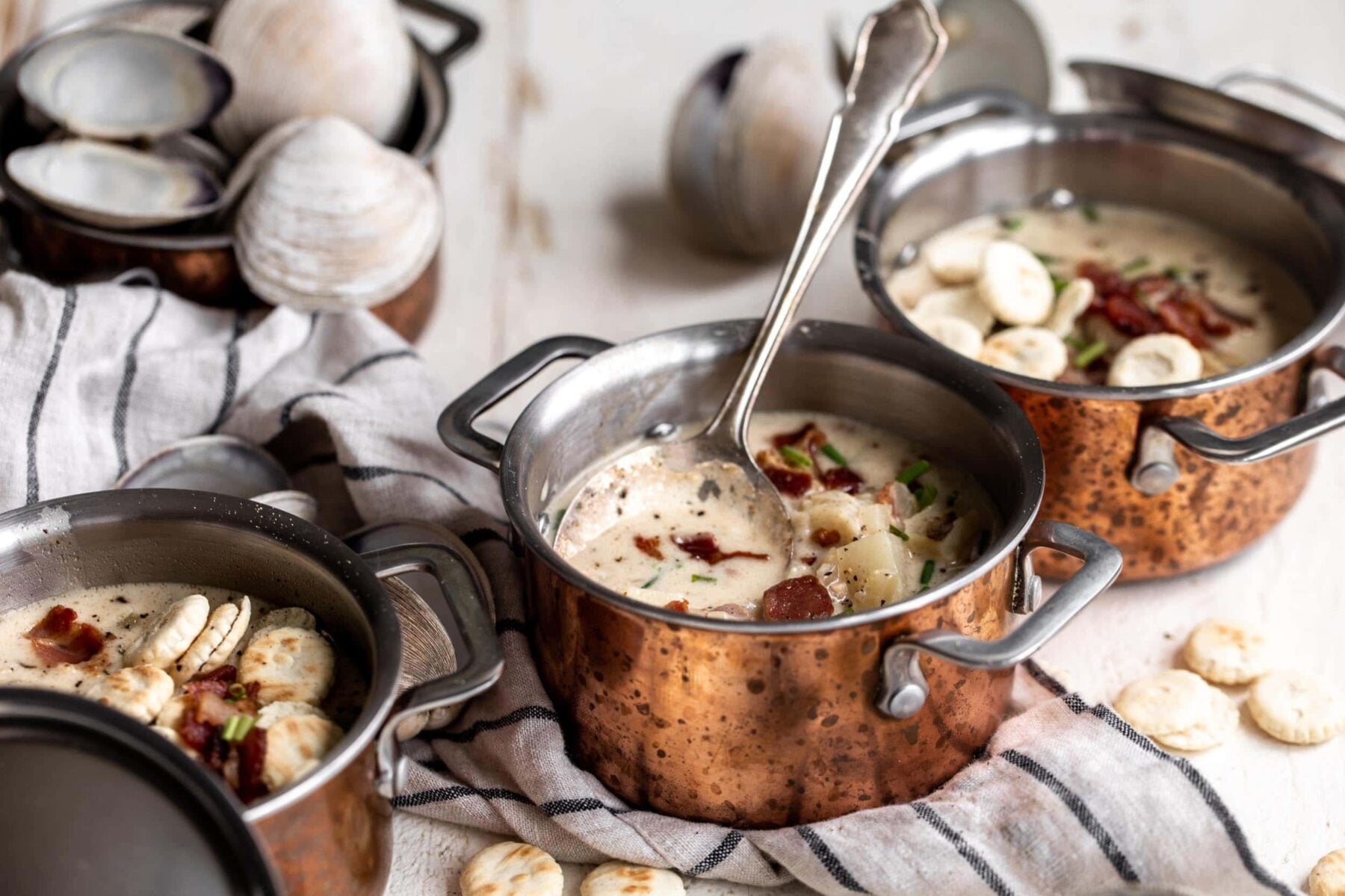 new england clam chowder in small copper pots with spoon and oyster crackers.
