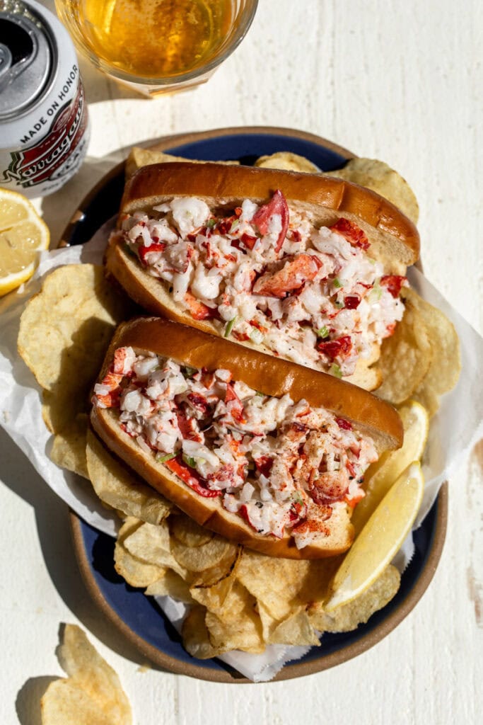 new england style lobster rolls in brioche buns with chips and lemon wedges.