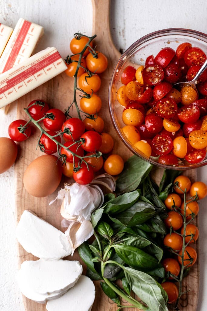 ingredients for caprese eggs benedict on wood cutting board.