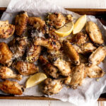 lemon pepper wings arranged on baking sheet with white parchment paper and lemon wedges