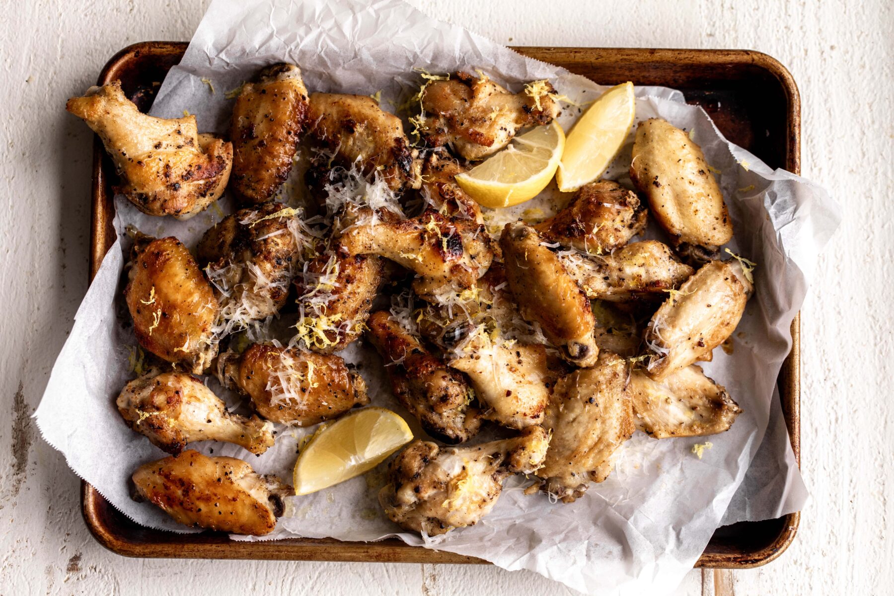 lemon pepper wings arranged on baking sheet with white parchment paper and lemon wedges.