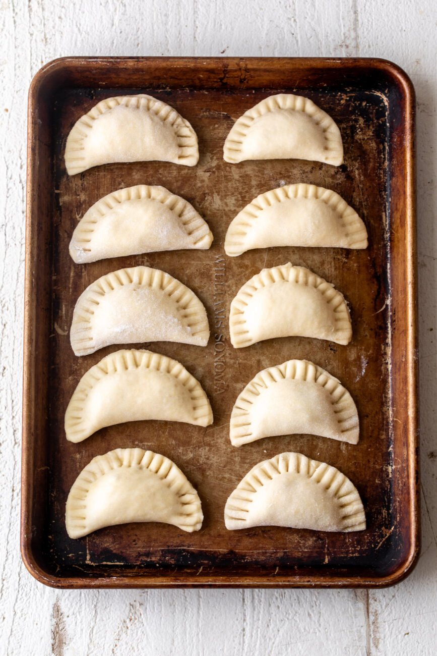 half moon shaped pierogi on baking sheet.