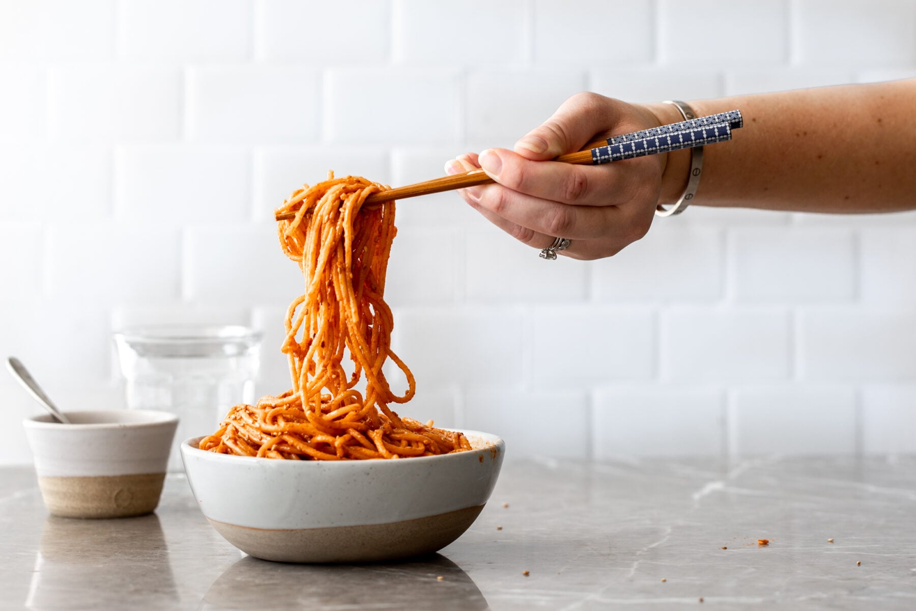 creamy gochujang noodles in bowl with chopsticks in hand lifting.